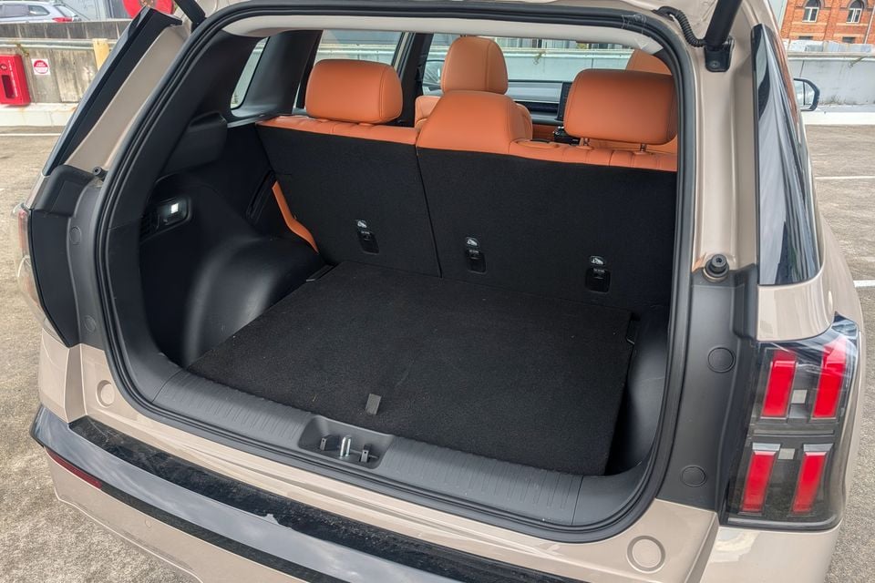 Open boot of a GAC Aion V SUV showing a spacious cargo area with black carpet, rear seat fold-down controls, and tan leather rear seats visible