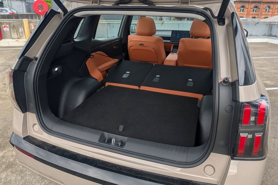 Boot of a GAC Aion V SUV open in a car park, showing a large flat cargo area with rear seats folded down and tan leather interior visible