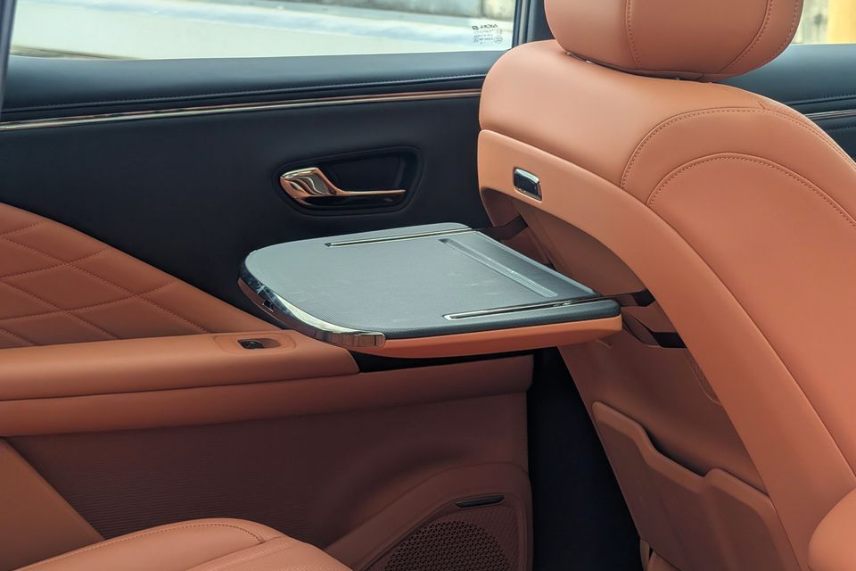 Rear passenger compartment of the GAC Aion V showing a fold-out tray table extended from the front seat back, with tan leather seats and dark door trim