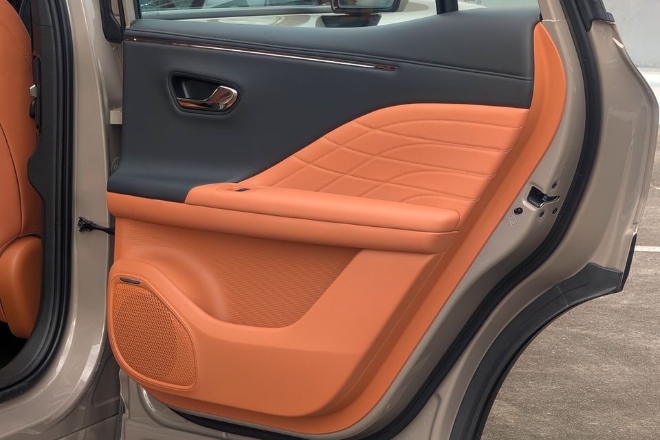 The open rear door of a GAC Aion V showing an orange and dark grey leather door trim panel with quilted stitching and a speaker grille