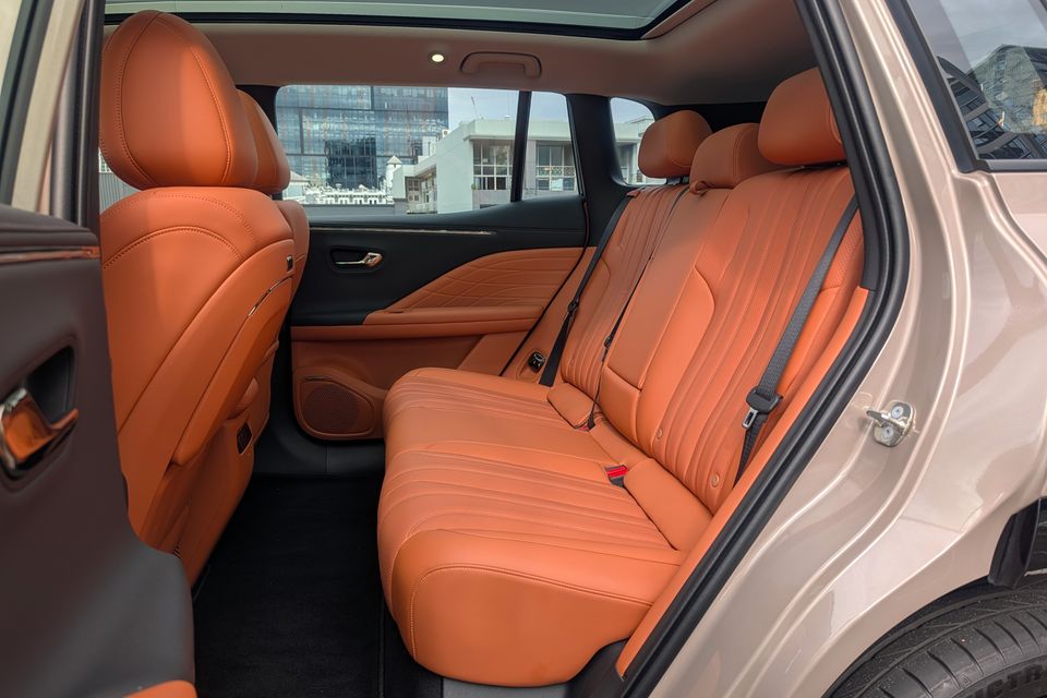 The tan leather rear seats of a GAC Aion V SUV, viewed from the open rear door, showing quilted upholstery and three-seat bench with seatbelts