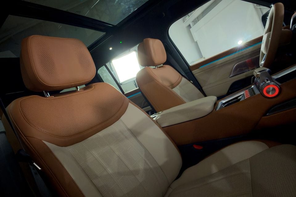 Interior of a 2027 Geely Battleship 700 showing tan and cream leather front and rear seats with ambient lighting and a panoramic sunroof