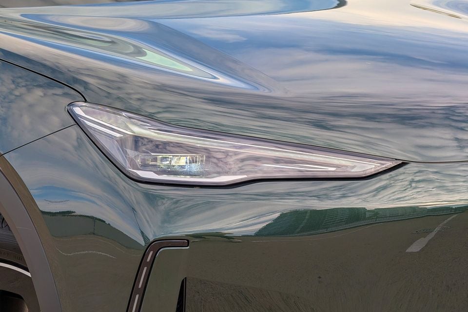 Close-up of the sleek LED headlight on a dark green Geely GX5, showing sharp angular styling and light strip detail.