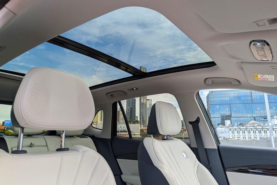 Interior view of a car's rear seating area showing white leather seats and a large panoramic sunroof with a city skyline visible through the windows