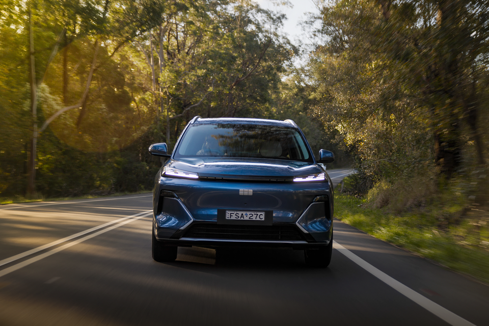 A blue 2027 Geely Starray EM-i SUV driving towards the camera on a tree-lined road