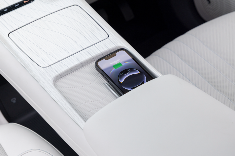 Centre console of the 2027 Geely Starray EM-i with a smartphone on the wireless charging pad, white woodgrain trim and light grey seats