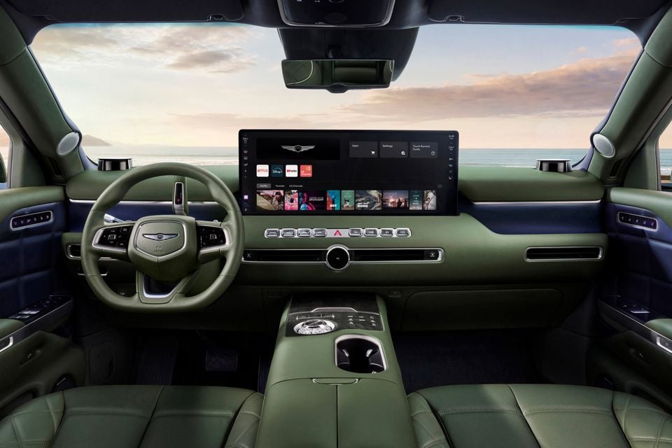 Interior of a 2027 Genesis GV90 showing a green leather dashboard, large central touchscreen displaying streaming apps, and a flat-bottomed steering wheel with the Genesis logo