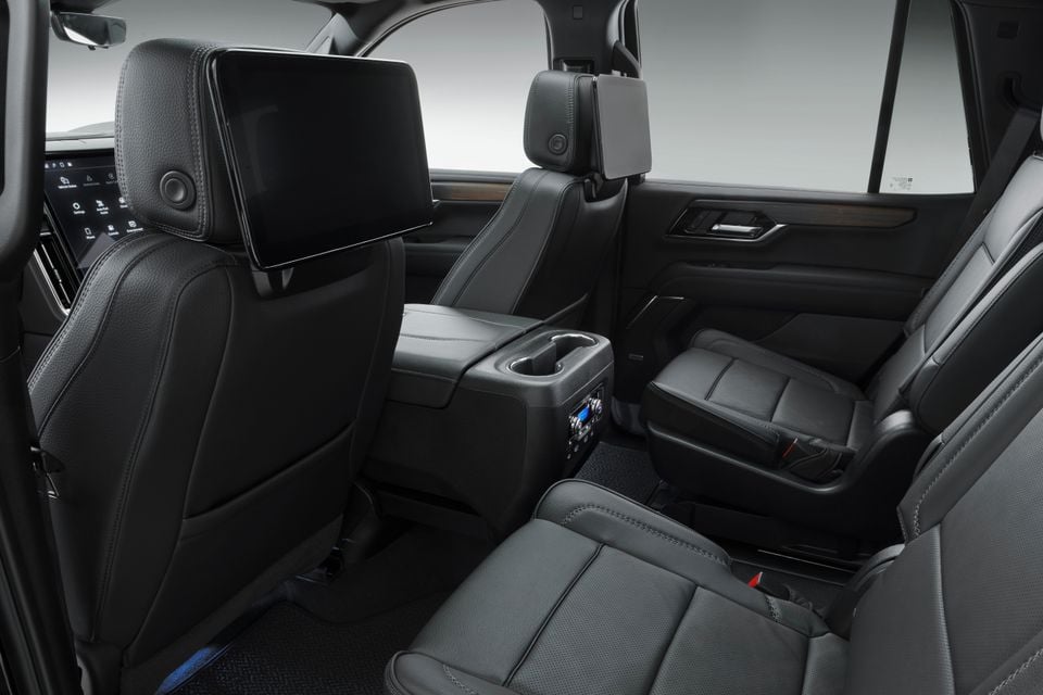 Interior rear seating area of a 2027 GMC Yukon Denali, showing black leather seats with a centre console, rear entertainment screen on the headrest, and rear-seat controls