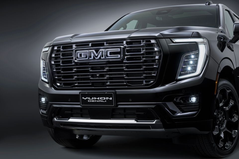 Close-up of the front grille and headlights of a black GMC Yukon Denali SUV in a studio setting