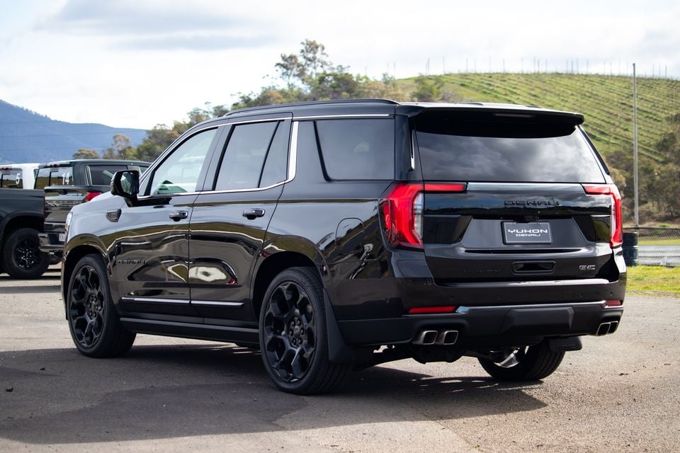 A black GMC Yukon Denali large SUV seen from the rear three-quarter angle, parked outdoors with hills in the background