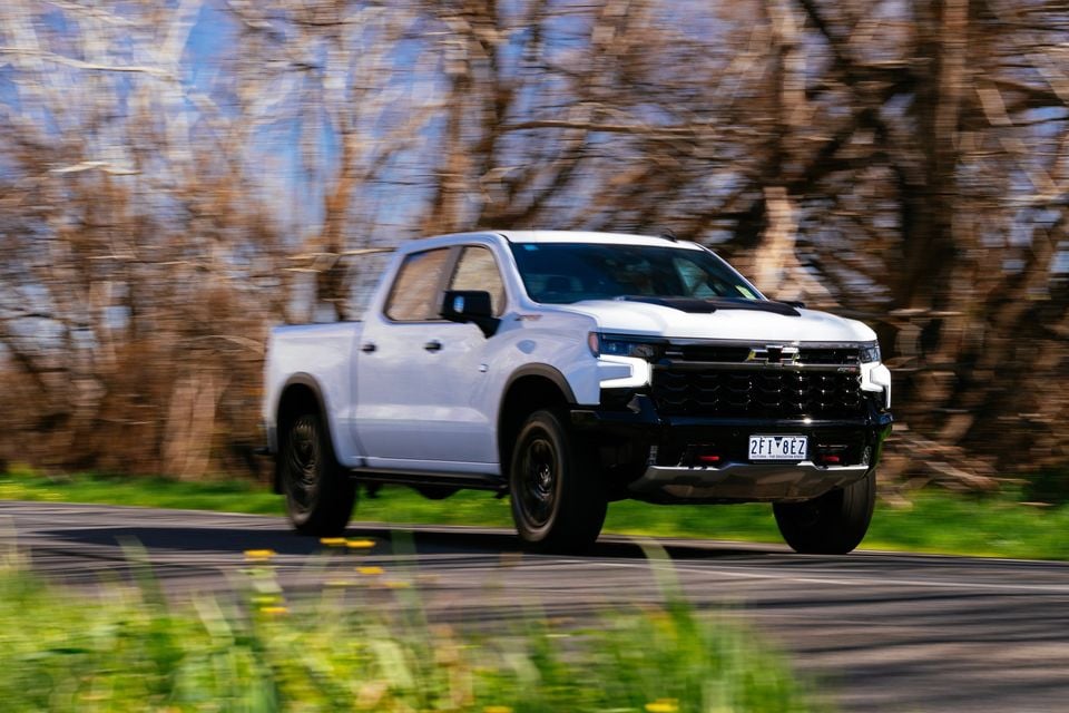 A white Chevrolet Silverado ZR2 ute driving along a tree-lined road, seen from the front-side