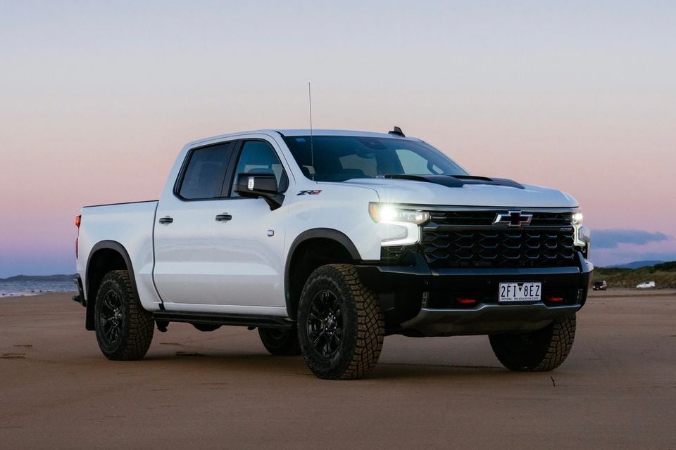 A white Chevrolet Silverado ZR2 crew cab ute parked on a beach at dusk, seen from the front-left side