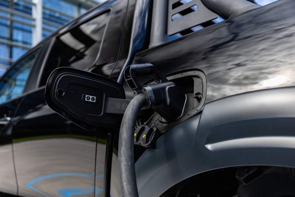 A charging cable plugged into the charge port of a dark-coloured GWM Cannon Hi4-T PHEV ute, with the side mirror visible in the background