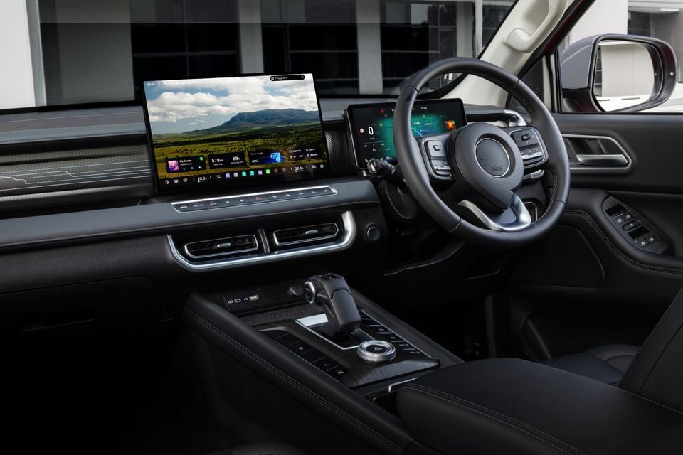 Interior of a GWM Cannon Hi4-T PHEV showing the large touchscreen infotainment display, digital instrument cluster, steering wheel, centre console and gear selector