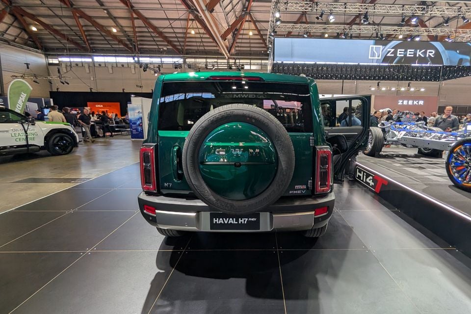 Rear view of a green Haval H7 PHEV SUV with a spare wheel mounted on the tailgate, displayed at a motor show