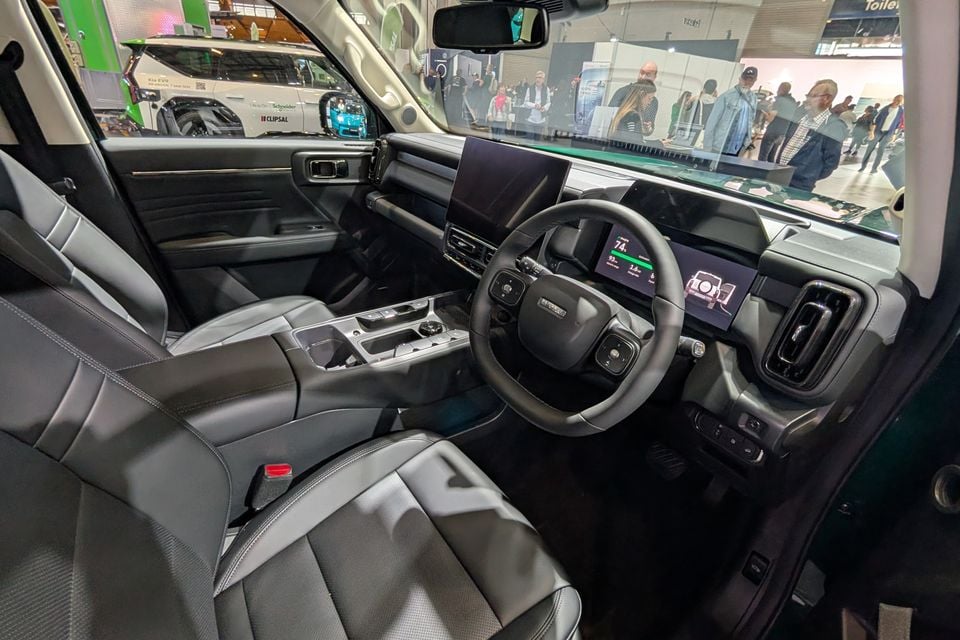 Interior of a GWM Haval H7 showing the dashboard, steering wheel, large central touchscreen, digital instrument cluster and grey leather seats, photographed at an auto show
