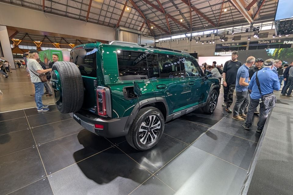 A green GWM Haval H7 SUV displayed at a motor show, seen from the rear three-quarter angle with a spare wheel mounted on the tailgate, surrounded by visitors