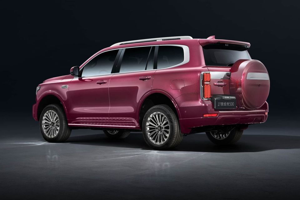 A pink 2027 GWM Tank 500 SUV seen from the rear three-quarter angle in a dark studio, showing its tailgate-mounted spare wheel