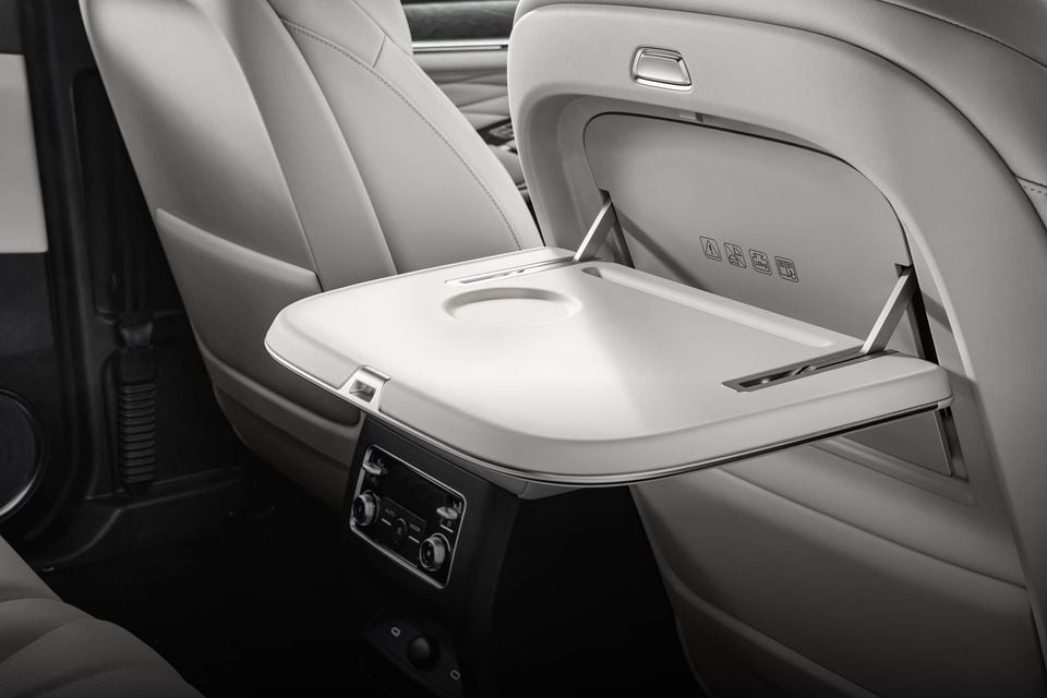 Fold-out tray table with cupholder on the back of a front seat in the 2027 GWM Tank 500, above rear climate controls in a light grey cabin