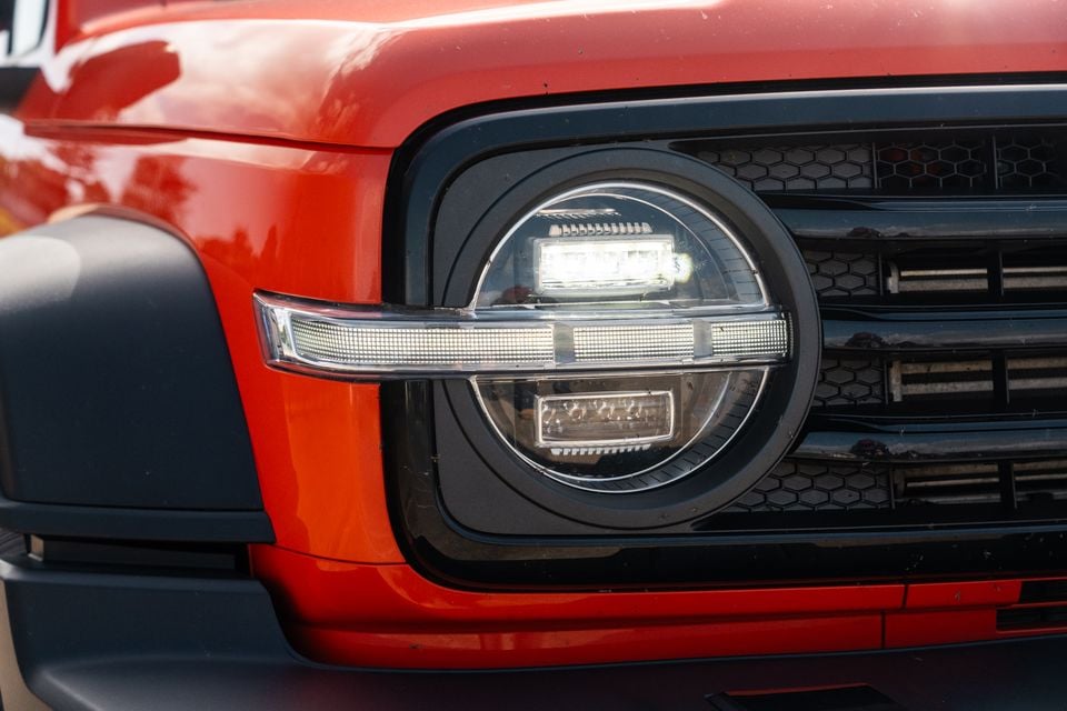Close-up of the round LED headlight and front grille of a red GWM Tank 300 Ultra PHEV