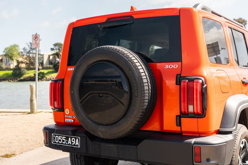 Rear view of an orange GWM Tank 300 PHEV 4WD SUV with a mounted spare tyre, parked near a waterfront in Australia
