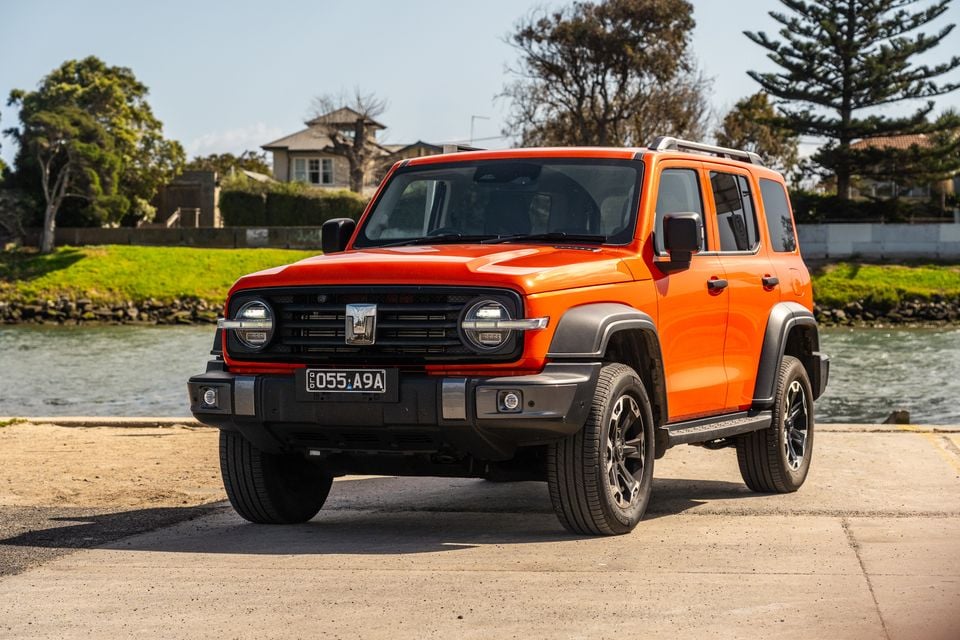 An orange GWM Tank 300 Ultra PHEV SUV seen from the front-side angle, parked near a waterway in Australia