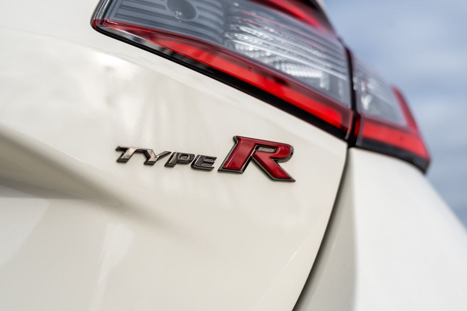 Close-up of the Type R badge on the rear quarter panel of a white Honda Civic Type R, with a tail light visible above.