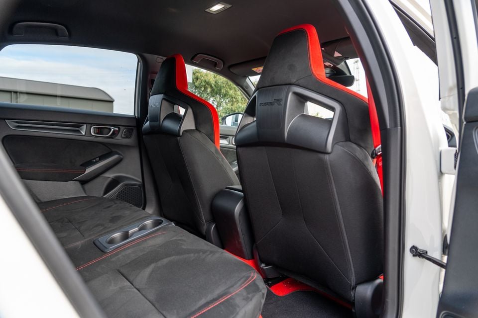 Interior rear view of a Honda Civic Type R showing black bucket front seats with red accents and Type R badging, and the rear bench seat with red stitching