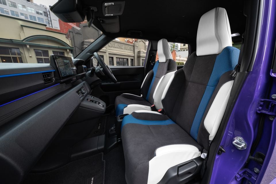 The front seats and dashboard of a 2027 Honda Super One, with black, white and blue upholstery and a purple exterior visible through the open door.