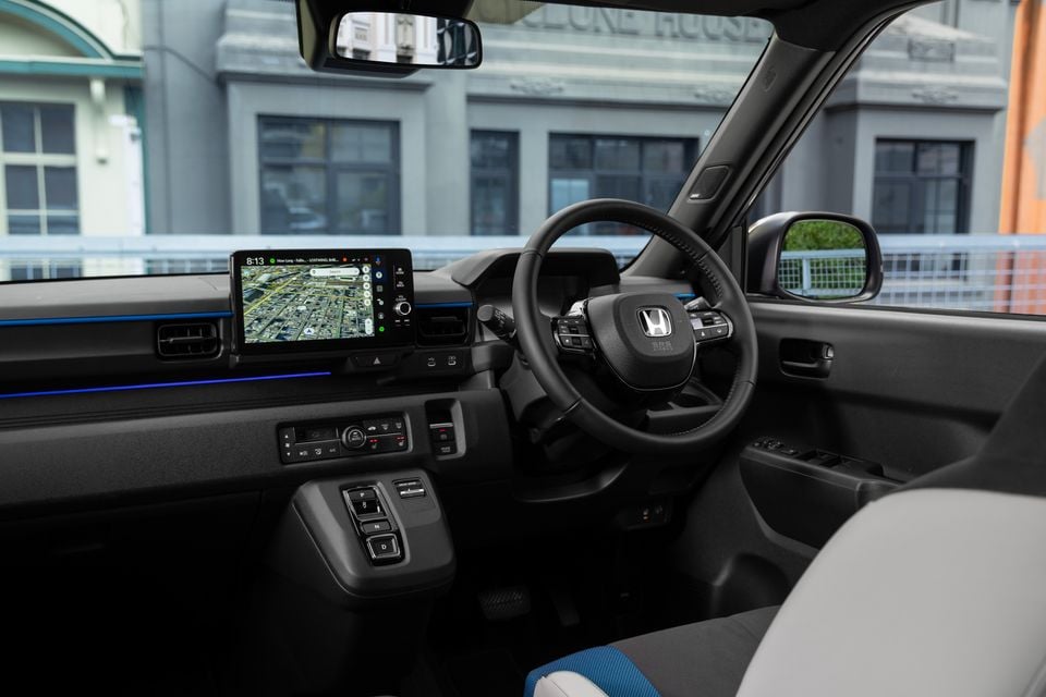 The interior of a 2027 Honda Super One shows the steering wheel, dashboard and touchscreen infotainment display with a map view.