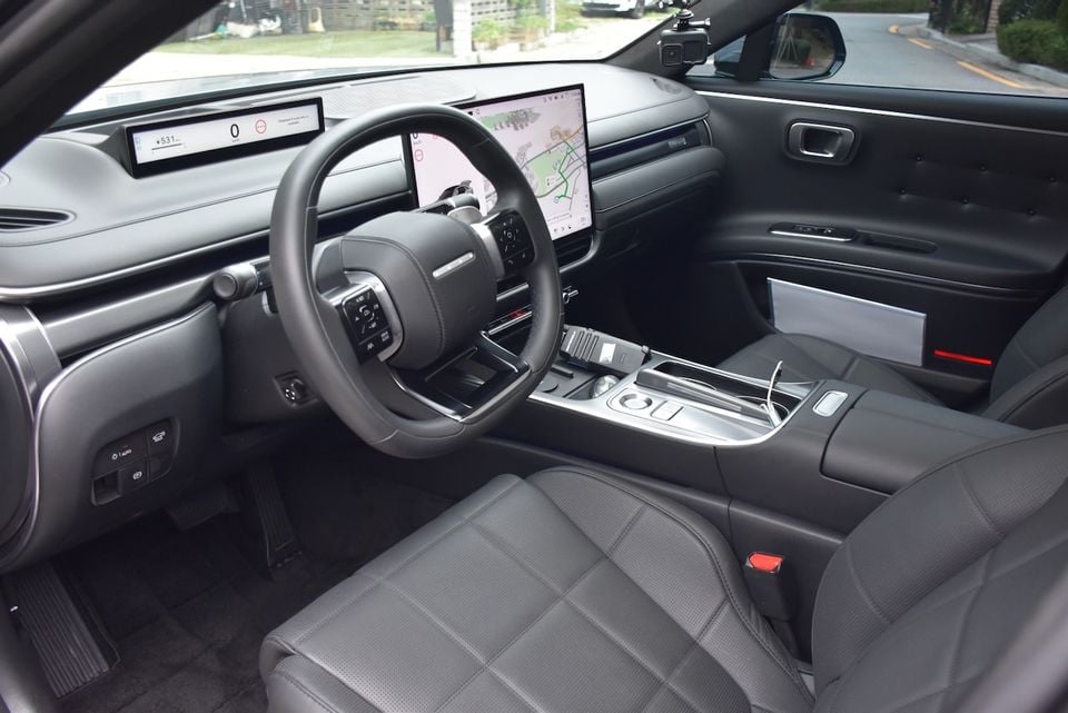 Interior of the 2027 Hyundai Grandeur showing the steering wheel, large central touchscreen displaying navigation, digital instrument cluster, centre console, and dark leather seats