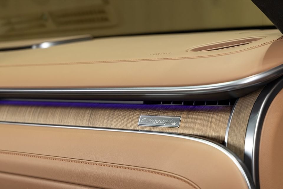 Close-up of the dashboard trim panel in a Hyundai Grandeur Calligraphy, showing tan leather, wood-effect trim, ambient purple lighting, and a Calligraphy badge