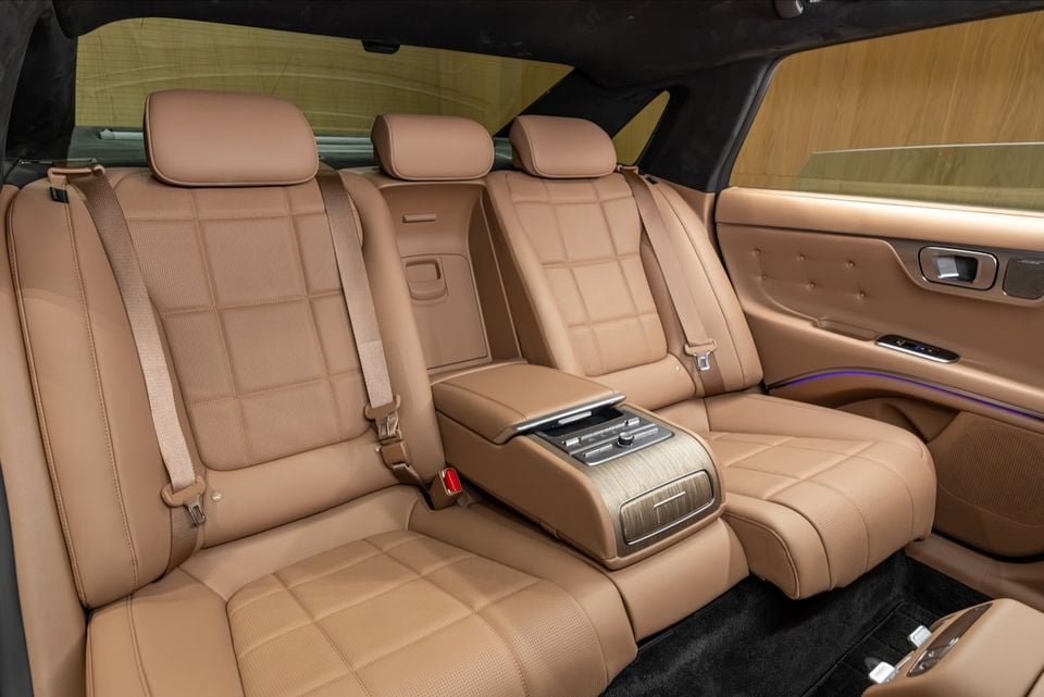 Luxury tan leather rear seats of the 2027 Hyundai Grandeur, showing quilted upholstery, a centre armrest with controls, and ambient lighting along the door trim.