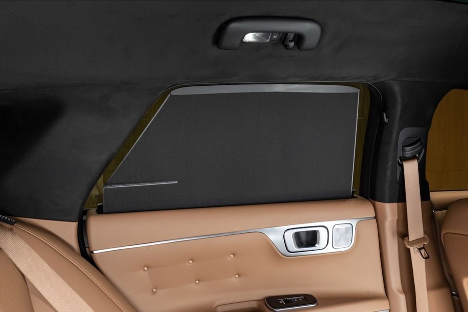 Interior rear door panel of a car showing a deployed window sun shade, tan leather trim with silver accents, and window controls