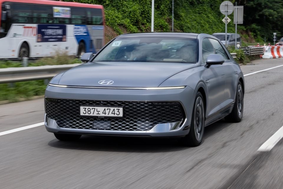 A grey Hyundai Grandeur sedan driving on a road, seen from the front