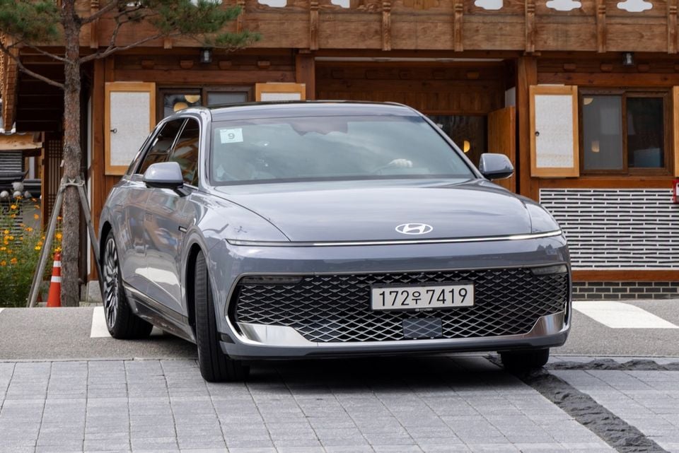 A grey Hyundai Grandeur sedan seen from the front, parked on a paved surface in front of a traditional Korean-style building.