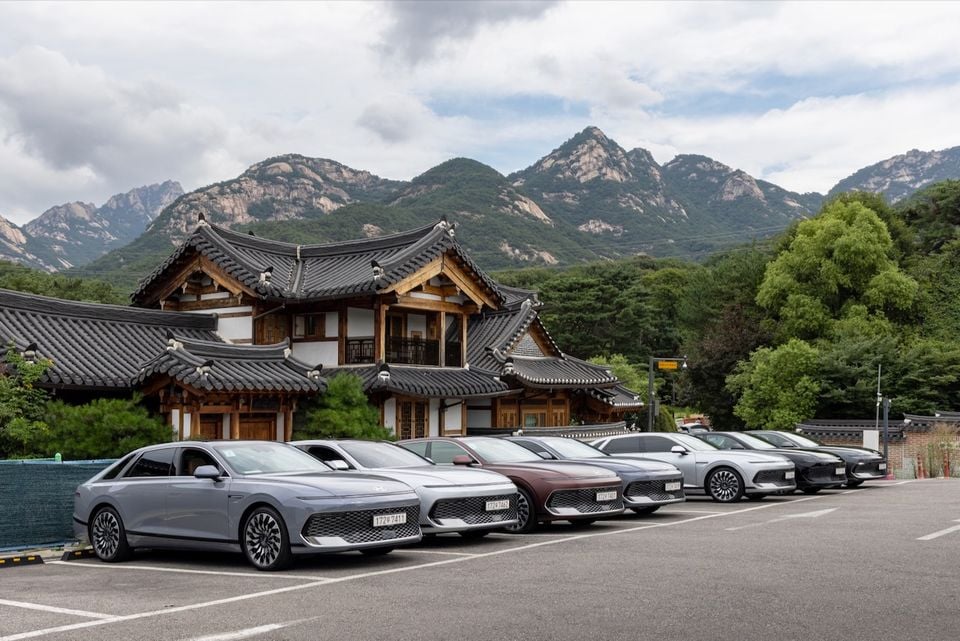 A lineup of Hyundai Grandeur sedans in various colours parked in front of a traditional Korean hanok building with mountain scenery in the background
