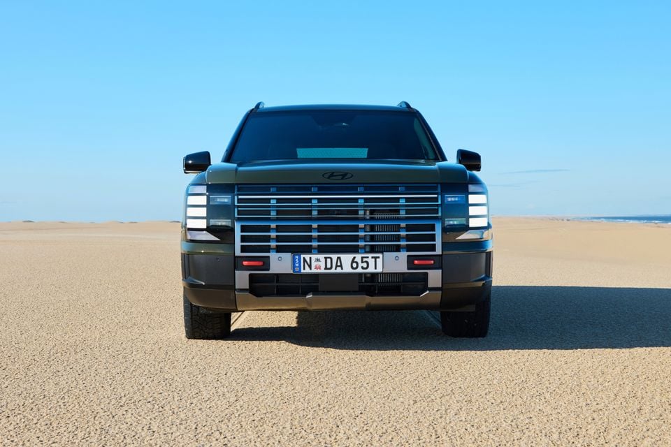 A dark green 2027 Hyundai Palisade XRT Pro SUV seen from the front, parked on a sandy beach under a clear blue sky.