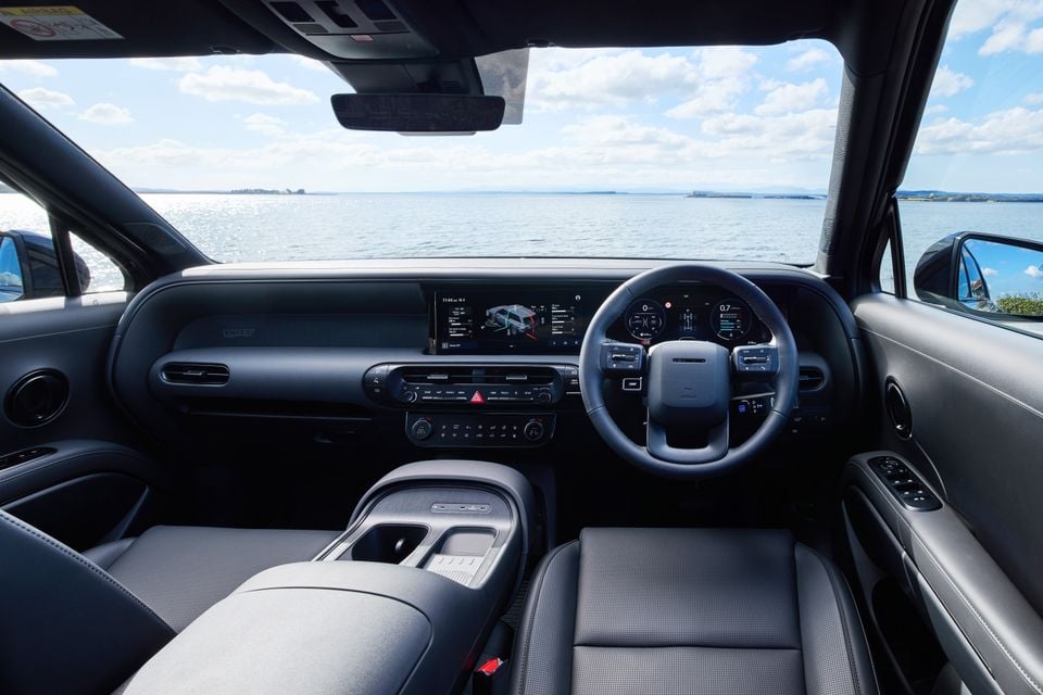 Interior of a 2027 Hyundai Palisade XRT Pro showing the dashboard, widescreen infotainment display, digital instrument cluster, steering wheel, and centre console, with a coastal water view through the windscreen