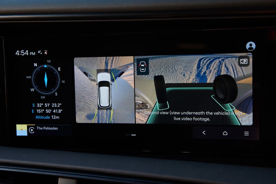 The infotainment screen of a 2027 Hyundai Palisade XRT Pro displaying a surround-view camera system with a bird's-eye view and ground view of the vehicle on a sandy terrain, alongside a compass and GPS coordinates.
