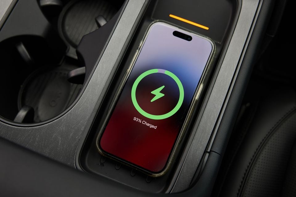 An iPhone wirelessly charging at 93% on the centre console wireless charging pad of a car interior