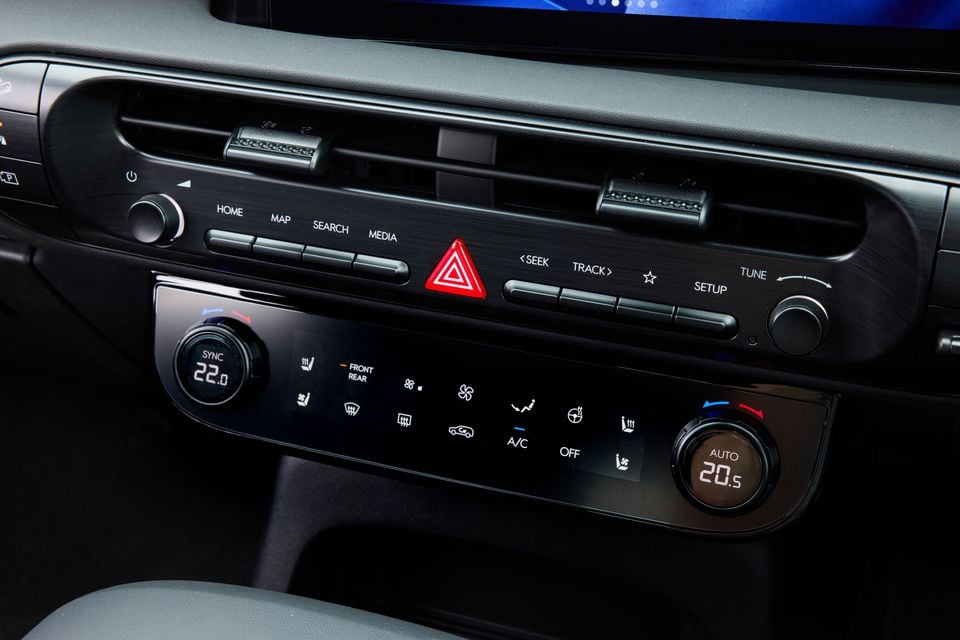Close-up of the centre console controls in a 2027 Hyundai Palisade XRT Pro, showing dual-zone climate control dials, air conditioning buttons, and infotainment shortcut controls with a red hazard button.