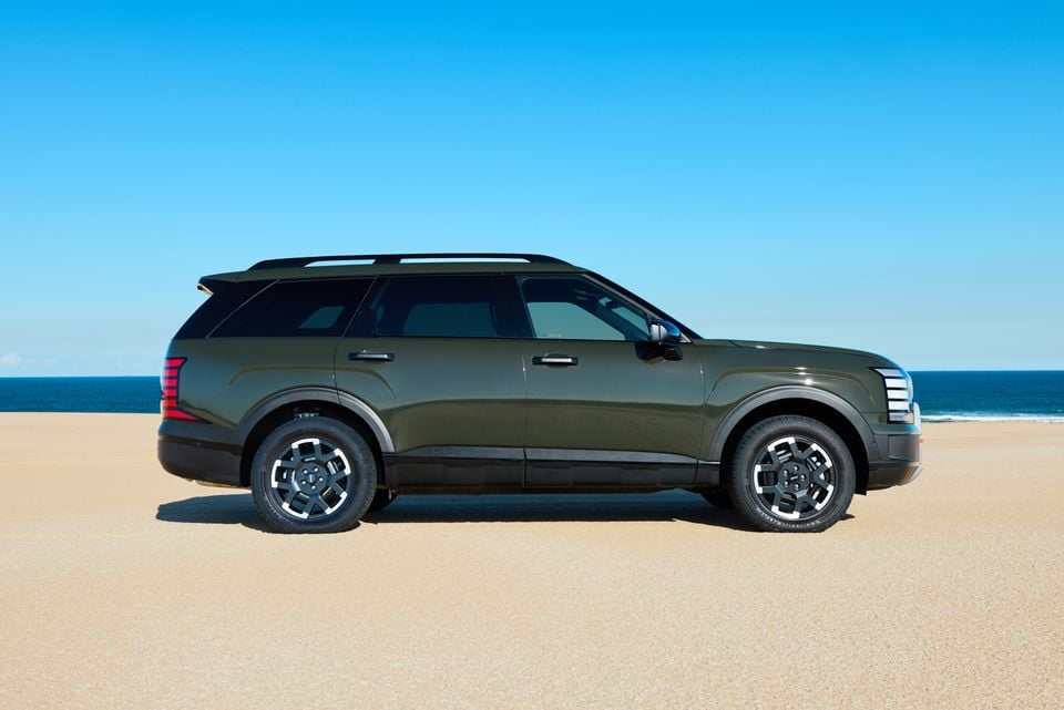 A dark green 2027 Hyundai Palisade XRT Pro large SUV seen from the side, parked on a sandy beach with the ocean in the background.