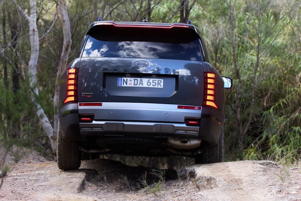 Rear view of a Hyundai Palisade XRT Pro SUV navigating a rocky off-road track surrounded by Australian bushland