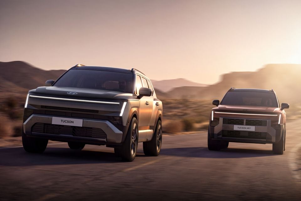 Two 2027 Hyundai Tucson SUVs — a standard Tucson and a Tucson XRT — driving on a desert road at sunset, seen from the front