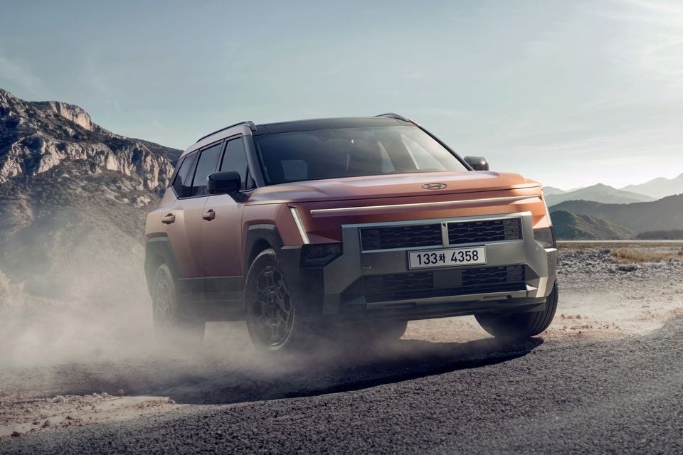 An orange 2027 Hyundai Tucson XRT SUV kicking up dust while driving on a dirt track with mountains in the background