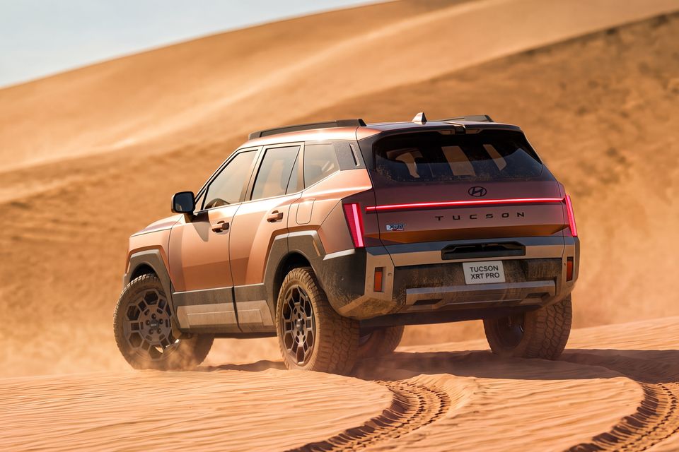 A bronze 2027 Hyundai Tucson XRT Pro SUV driving through desert sand dunes, seen from the rear quarter.