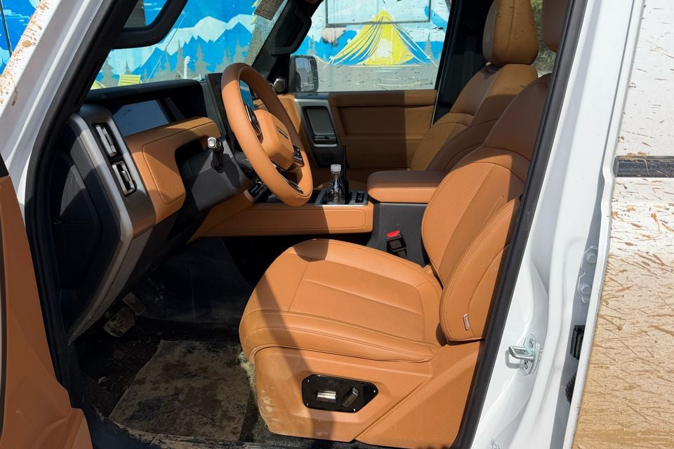 Cabine dianteira com volante à esquerda de um carro de teste iCaur V25 estrangeiro, com assentos bege, volante e console central.