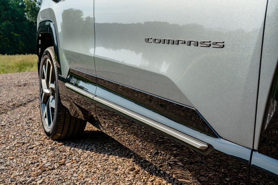 Close-up of the side panel and door sill of a silver Jeep Compass SUV, showing the 'Compass' badge and chrome trim strip
