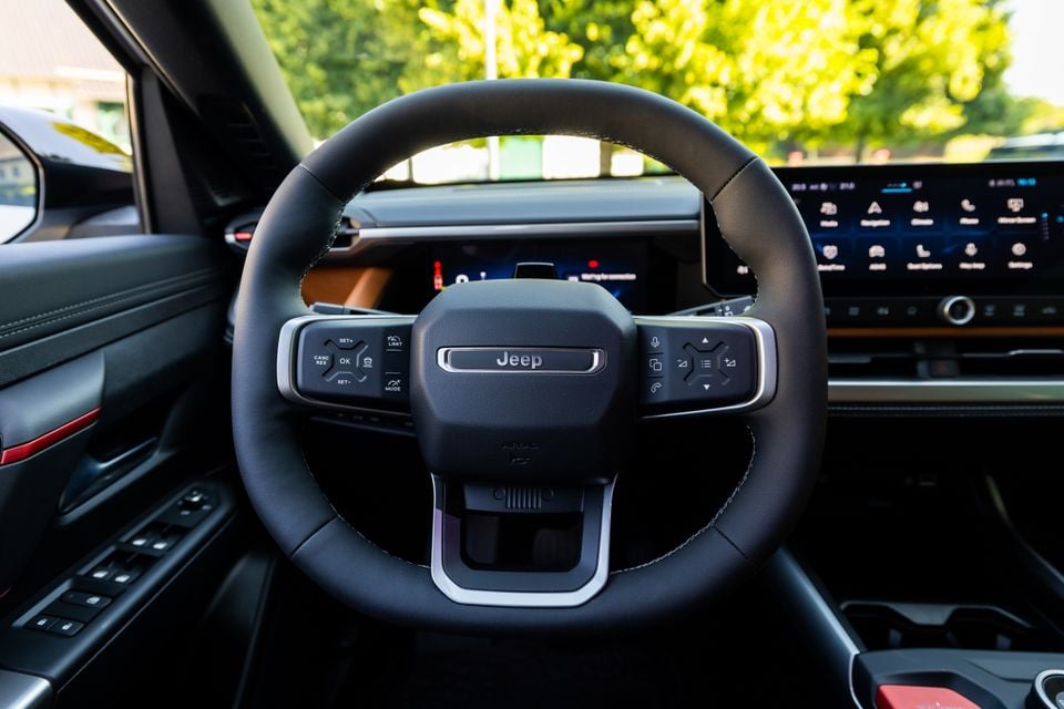The steering wheel and infotainment screen of a 2027 Jeep Compass, showing the Jeep-branded flat-bottom wheel with mounted controls and a large touchscreen display in the background.